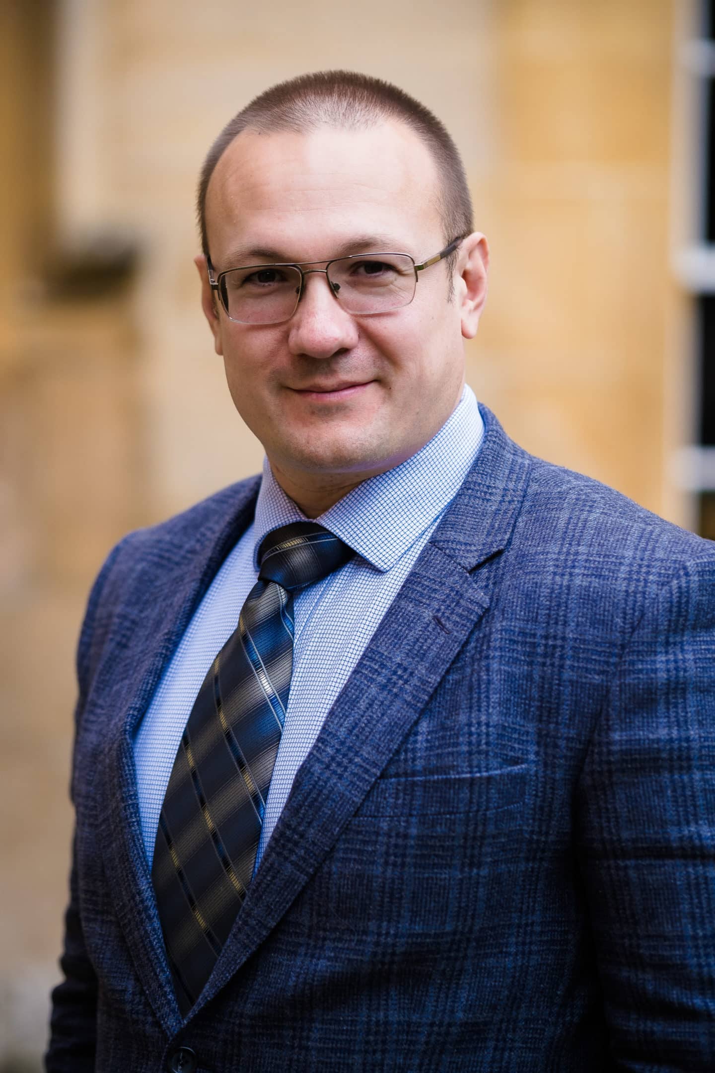 Headshot of Dr Alexei Parakhonyak, a man in glasses and a blue suit and tie