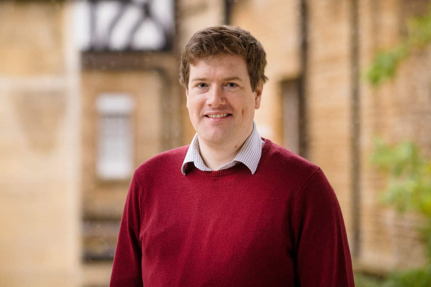 Headshot of Dr Sam Brewitt-Taylor, a man in a shirt and red jumper