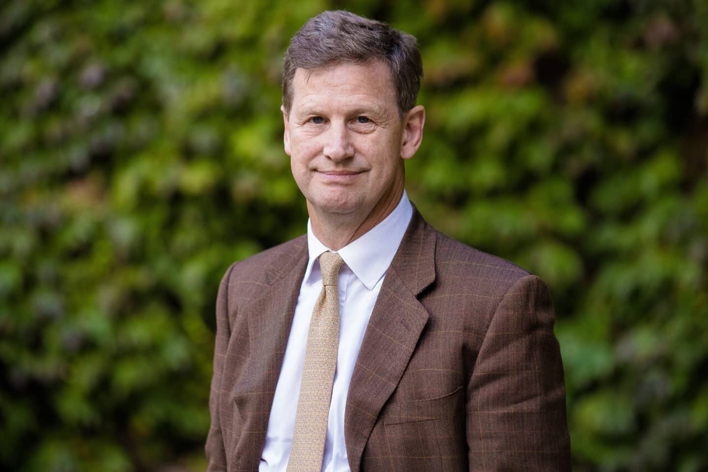 Headshot of Alex Spain, a man in a brown suit and tie