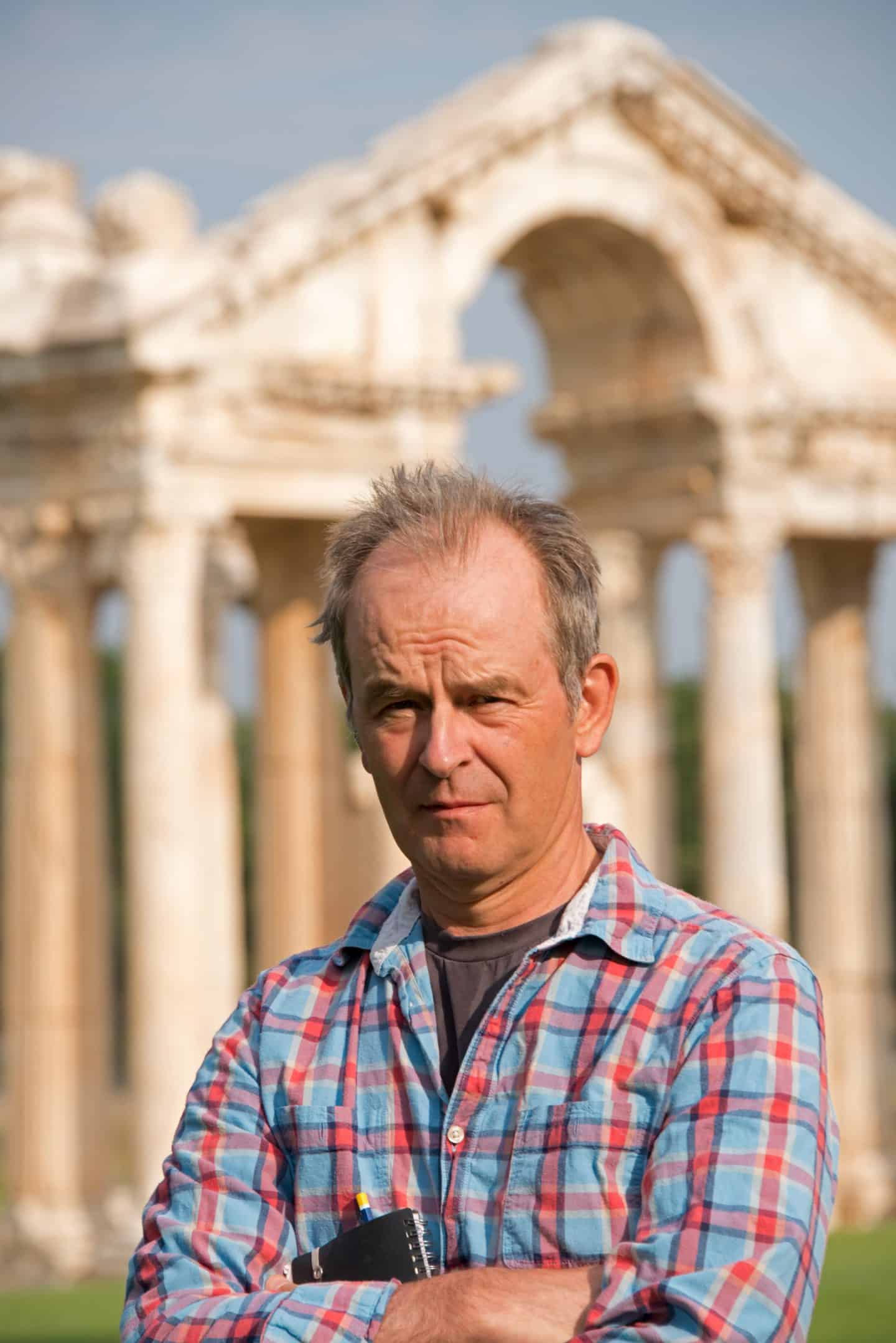 Photograph of Professor Bert Smith, a man in a shirt, holding a notebook, standing in front of some columns