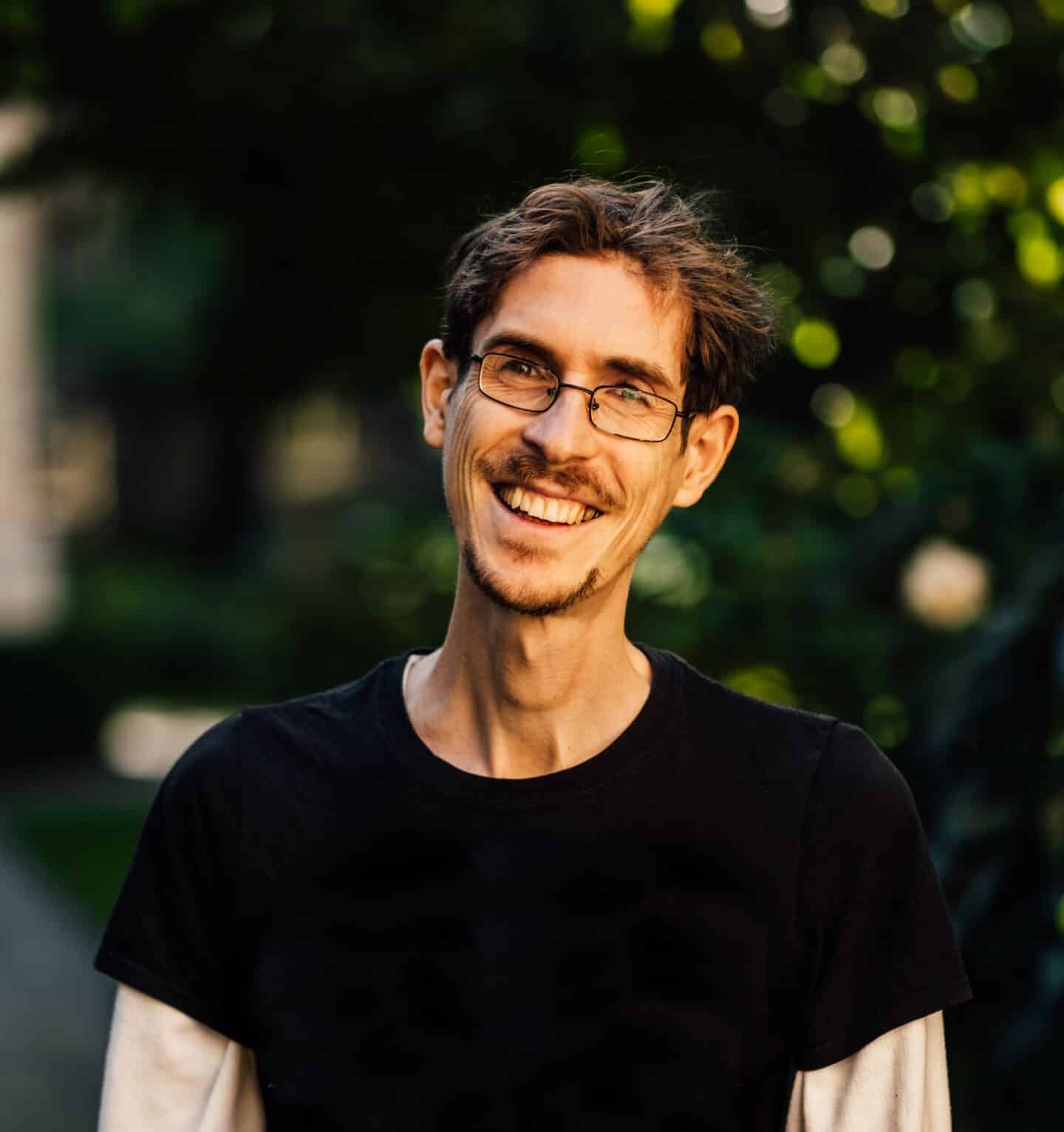 Headshot of Peter Sarkies, a smiling man in glasses and a black t-shirt