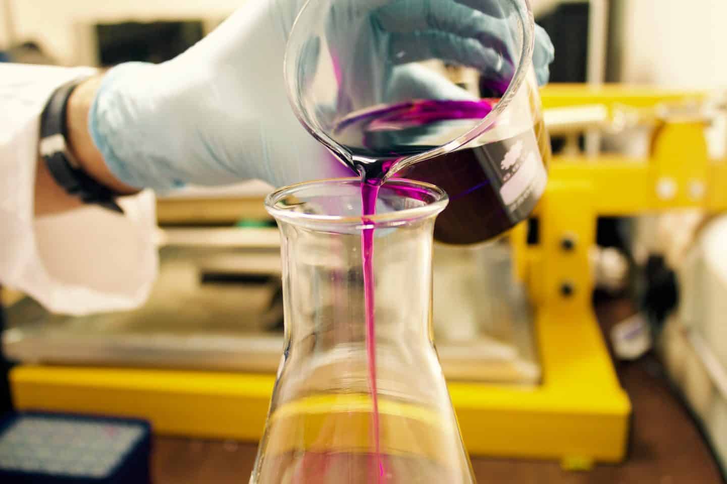 Image of a purple liquid being poured from one beaker into another in a Chemistry lab