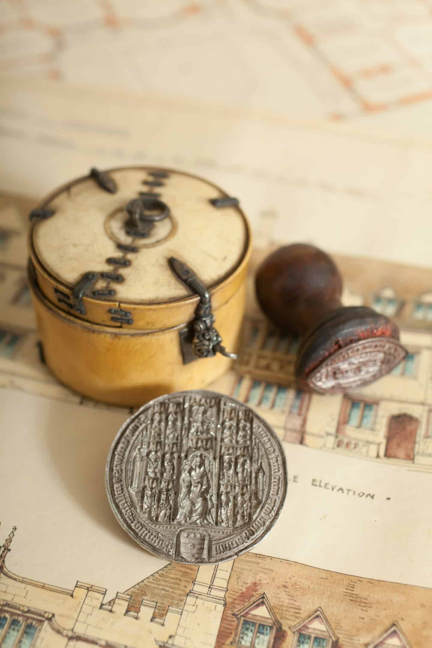 A wooden box with metal hinges, a circular silver seal, and a smaller wooden-handled seal