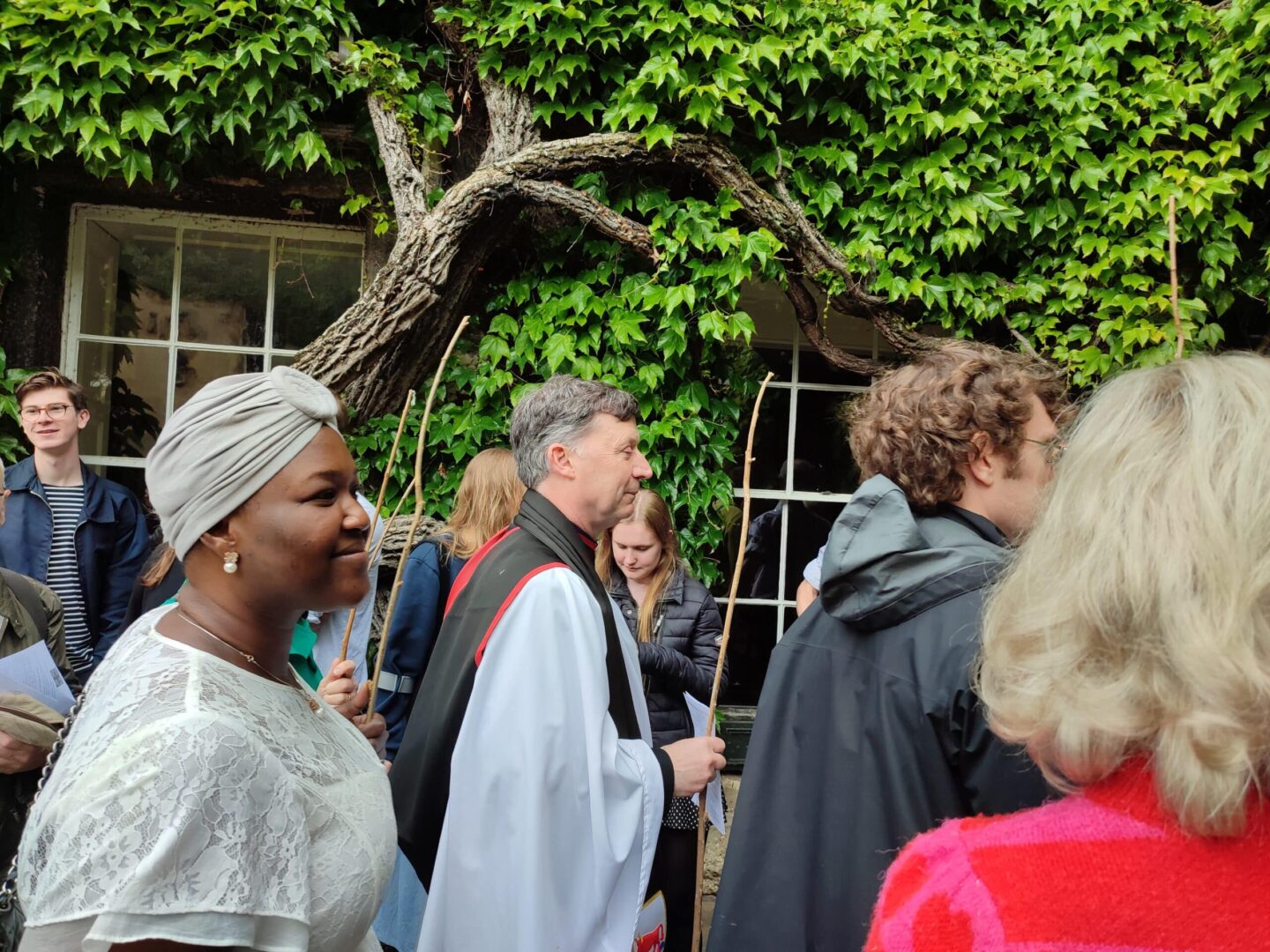A priest and congregation walking through the Front Quad of Lincoln College with large sticks to beat the bounds